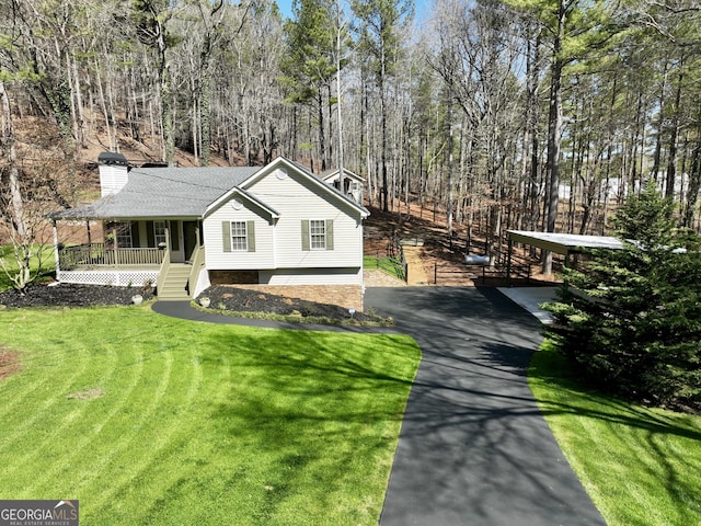 view of front of home featuring a chimney, a porch, a wooded view, and a front lawn