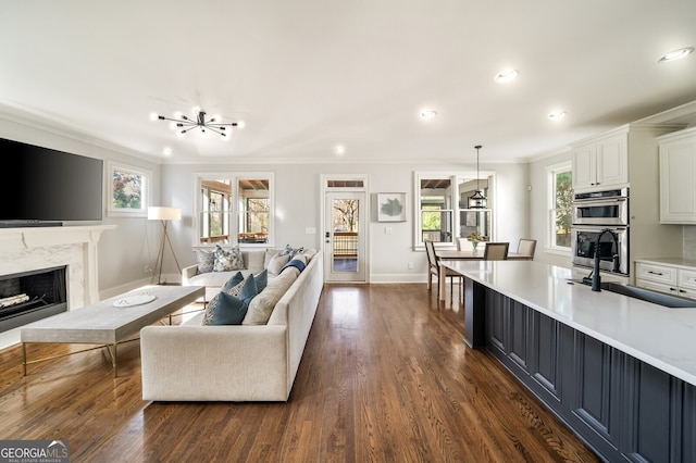 living area with baseboards, a premium fireplace, dark wood finished floors, an inviting chandelier, and ornamental molding