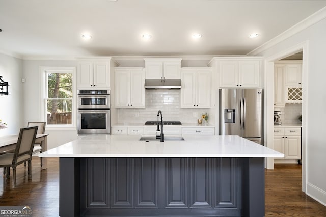 kitchen featuring a sink, under cabinet range hood, appliances with stainless steel finishes, white cabinetry, and a kitchen island with sink