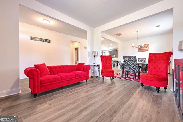 living room featuring an inviting chandelier, wood finished floors, visible vents, and baseboards