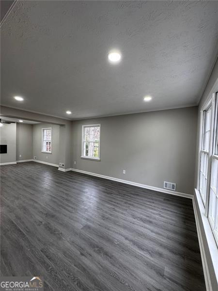 unfurnished room featuring dark wood finished floors, visible vents, a textured ceiling, and baseboards