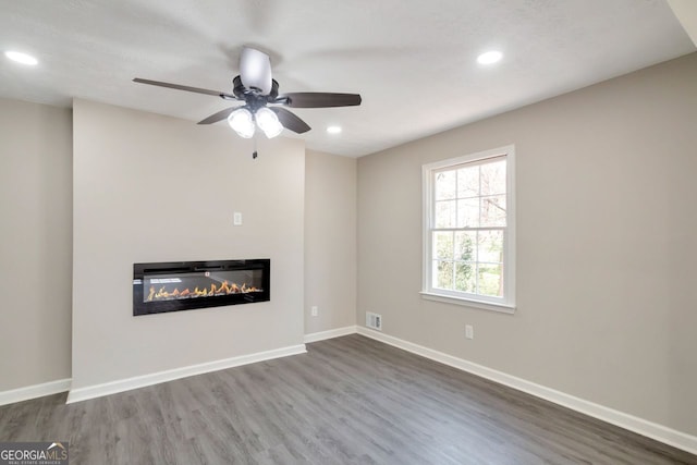 unfurnished living room featuring visible vents, baseboards, recessed lighting, wood finished floors, and a glass covered fireplace