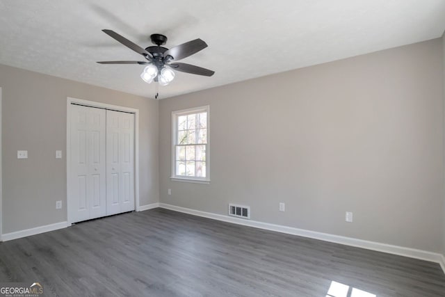 unfurnished bedroom featuring dark wood-style floors, baseboards, visible vents, and a closet