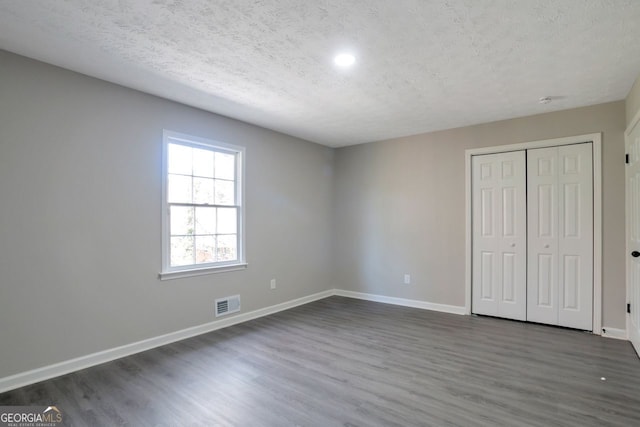 unfurnished bedroom featuring visible vents, dark wood-type flooring, a textured ceiling, and baseboards