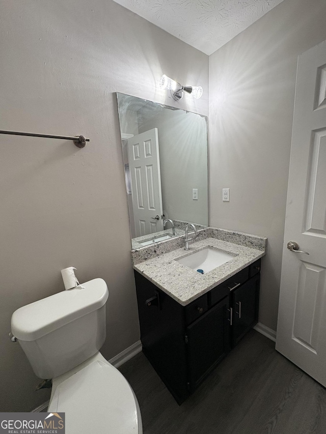 half bathroom featuring baseboards, toilet, vanity, wood finished floors, and a textured ceiling