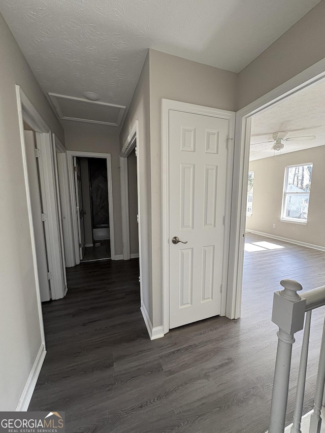 hallway featuring dark wood finished floors, attic access, and baseboards