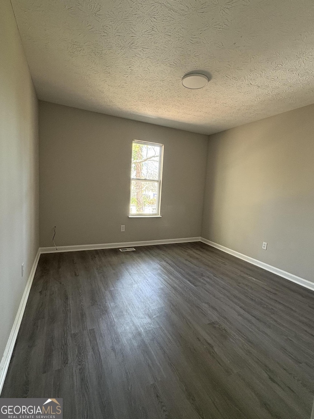 empty room featuring visible vents, baseboards, and dark wood-style flooring