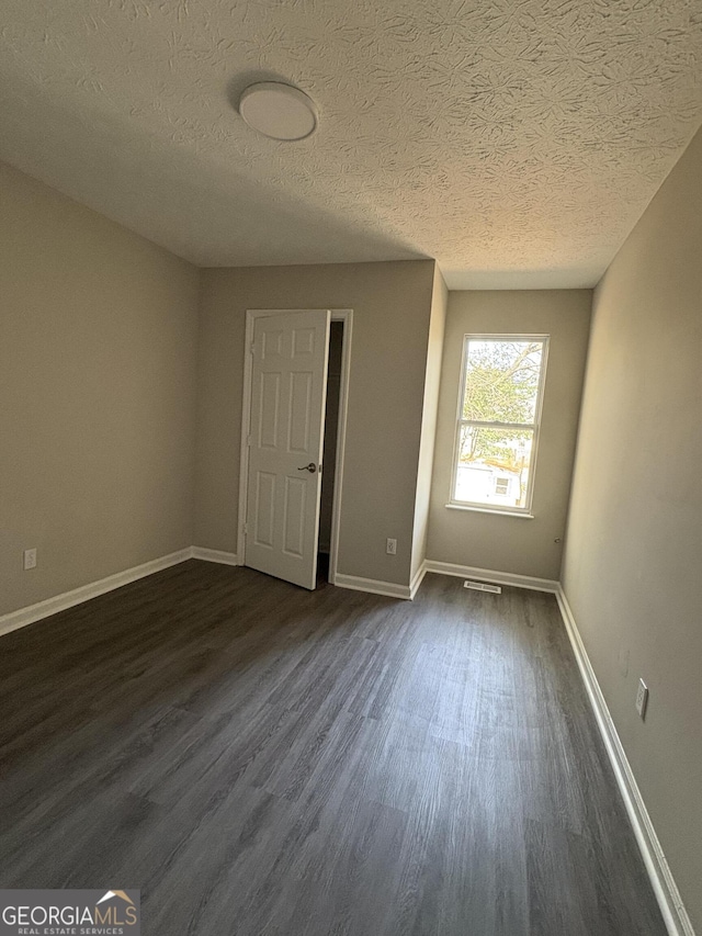 spare room featuring visible vents, a textured ceiling, dark wood-type flooring, and baseboards