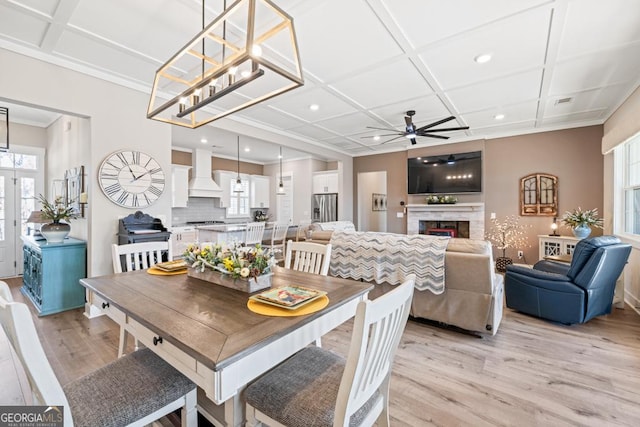 212 Cardiff Ct, Ball Ground, GA 30107 - dining space with light wood-style flooring, coffered ceiling, a ceiling fan, crown molding, and a warm lit fireplace