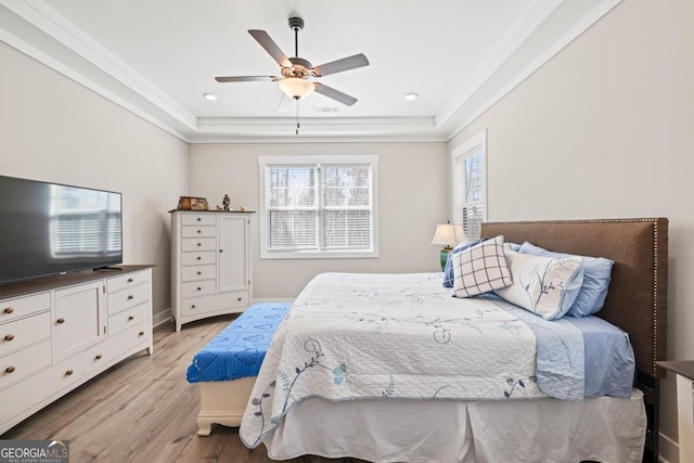 bedroom with ceiling fan, a raised ceiling, crown molding, and light wood-style floors