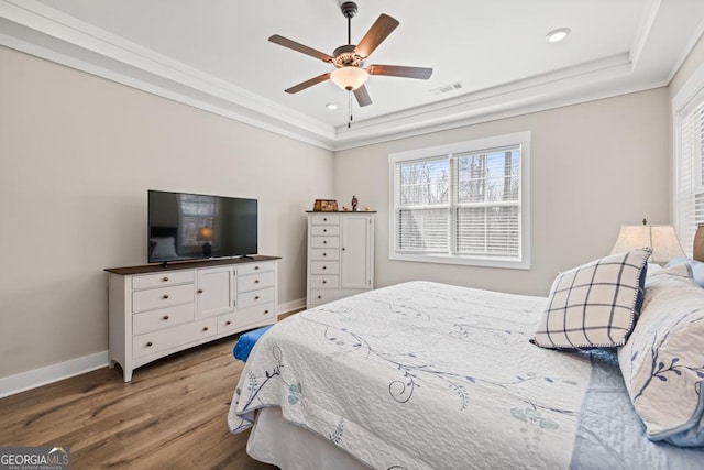 bedroom with wood finished floors, baseboards, visible vents, crown molding, and a raised ceiling