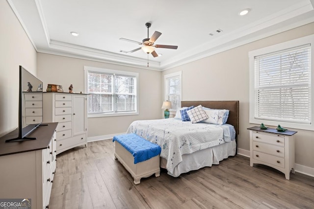 bedroom featuring light wood-style flooring, a raised ceiling, baseboards, and ornamental molding