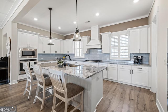 kitchen featuring white cabinets, appliances with stainless steel finishes, custom range hood, and a sink