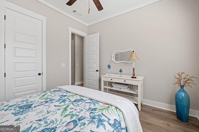 bedroom featuring a ceiling fan, wood finished floors, baseboards, visible vents, and crown molding