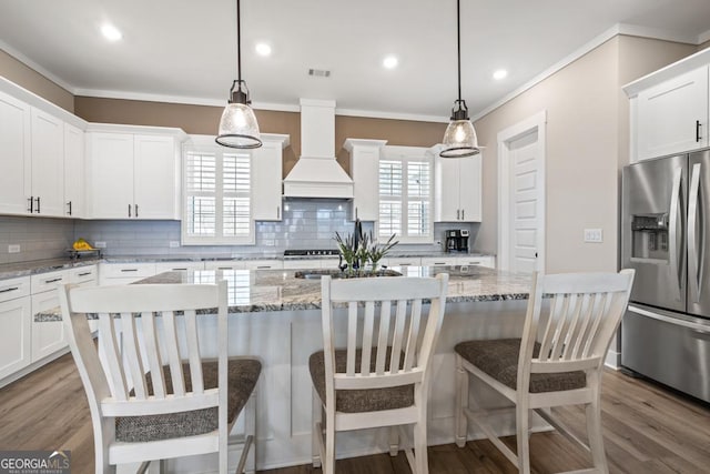 kitchen featuring stainless steel fridge with ice dispenser, ornamental molding, custom range hood, white cabinetry, and tasteful backsplash