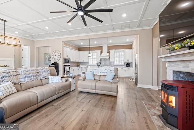 living area featuring light wood finished floors, ceiling fan with notable chandelier, coffered ceiling, and crown molding