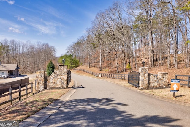 view of road featuring street lights, a gate, and a wooded view