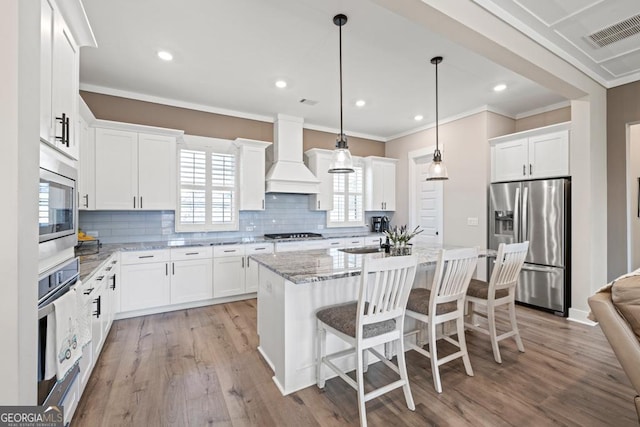 kitchen featuring visible vents, light wood-type flooring, custom range hood, decorative backsplash, and appliances with stainless steel finishes