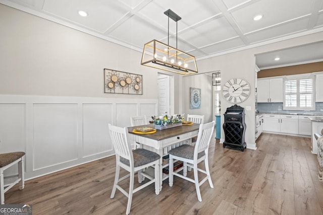 dining room featuring a wainscoted wall, coffered ceiling, a decorative wall, and light wood-style floors