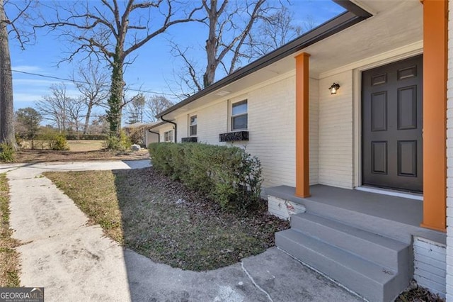 doorway to property featuring brick siding and covered porch