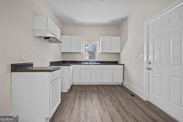 kitchen featuring visible vents, dark countertops, wood finished floors, white cabinetry, and baseboards