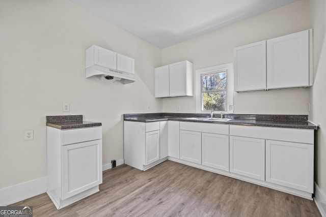 kitchen with light wood finished floors, dark countertops, baseboards, white cabinetry, and a sink