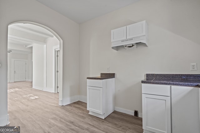 interior space featuring arched walkways, light wood-style flooring, and baseboards