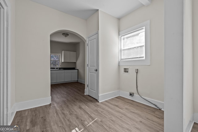 laundry area featuring arched walkways, light wood-style floors, baseboards, hookup for a washing machine, and laundry area