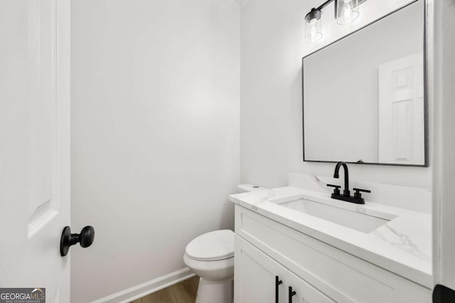 bathroom with baseboards, toilet, wood finished floors, and vanity