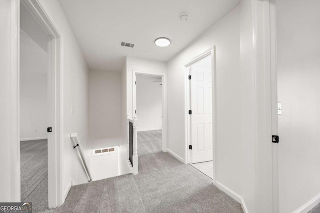 hallway featuring light colored carpet, an upstairs landing, visible vents, and baseboards