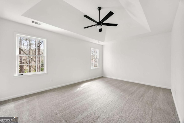 carpeted empty room with a tray ceiling, baseboards, and visible vents