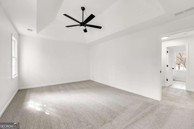 carpeted empty room featuring visible vents, baseboards, a raised ceiling, and a ceiling fan