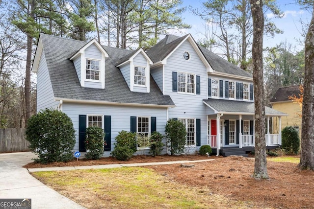 colonial home with covered porch, roof with shingles, and fence