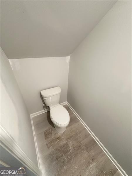 bathroom with vaulted ceiling, toilet, wood finished floors, and baseboards