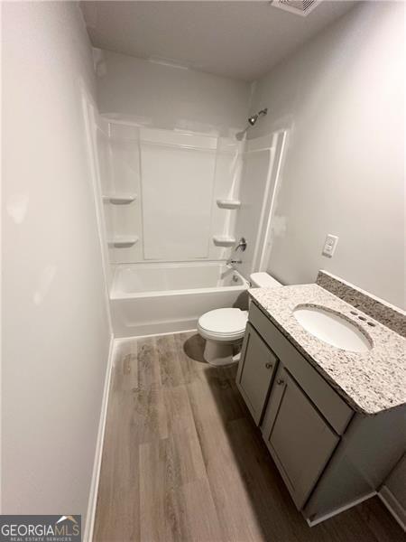 bathroom featuring shower / washtub combination, toilet, vanity, and wood finished floors