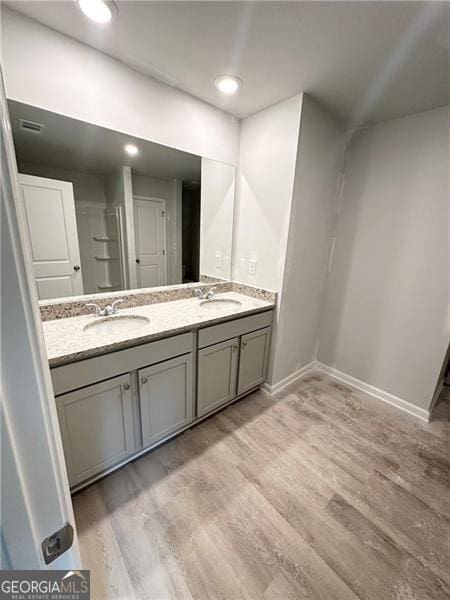 full bathroom with double vanity, a sink, baseboards, and wood finished floors