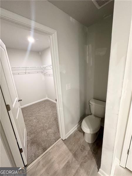 bathroom with a spacious closet, toilet, visible vents, and baseboards