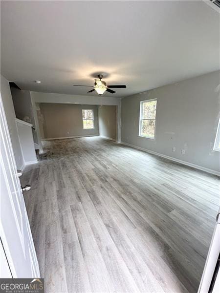 unfurnished living room featuring baseboards, wood finished floors, plenty of natural light, and ceiling fan