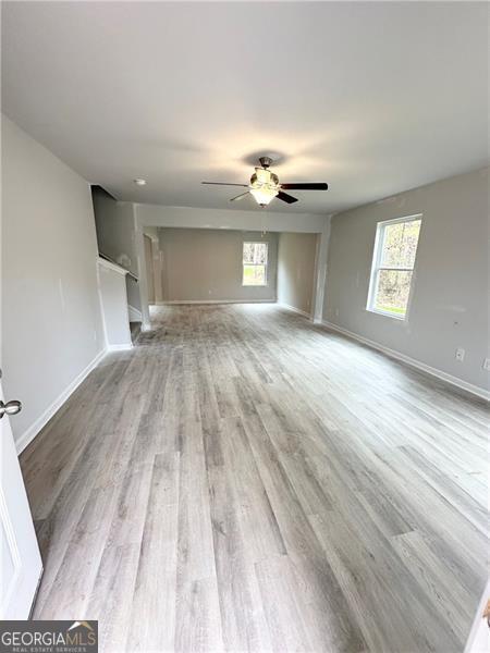 unfurnished living room featuring a wealth of natural light, baseboards, light wood-style floors, and a ceiling fan