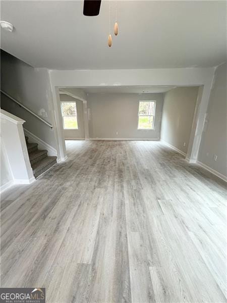 unfurnished living room with stairway, ceiling fan, baseboards, and wood finished floors