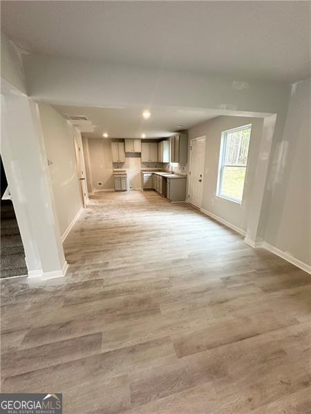 unfurnished living room with recessed lighting, baseboards, light wood finished floors, and a sink