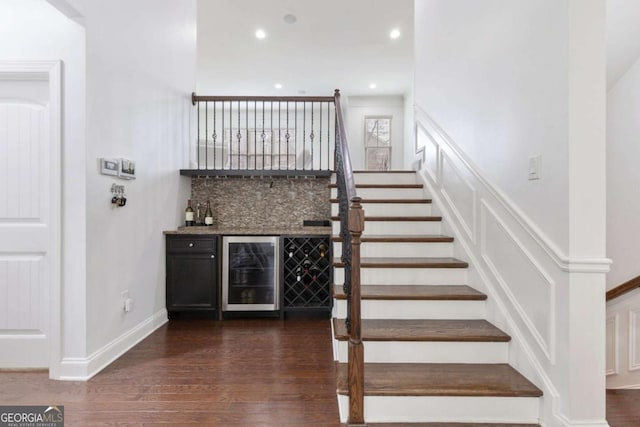 stairway with wood finished floors, recessed lighting, wine cooler, baseboards, and a dry bar