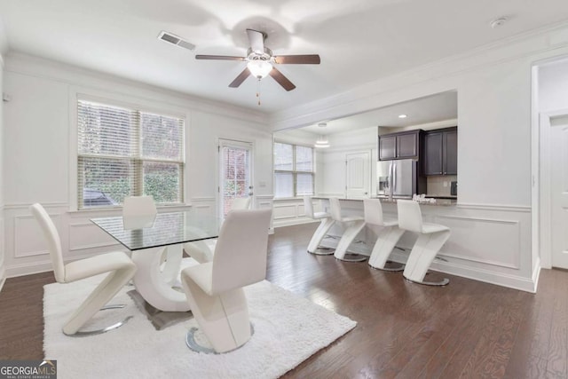 dining room featuring visible vents, ceiling fan, dark wood-type flooring, wainscoting, and a decorative wall