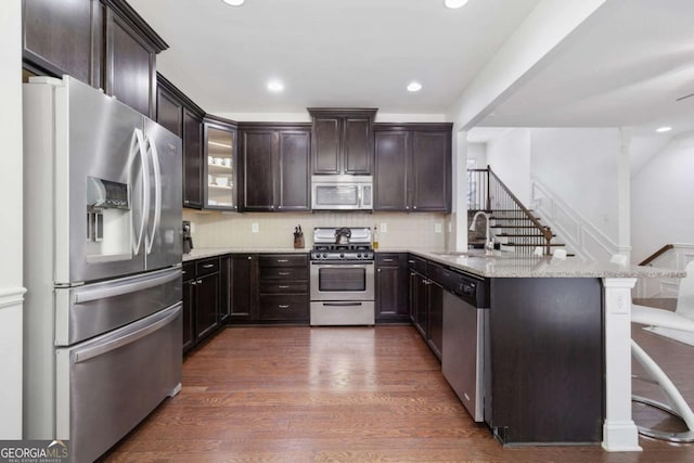 kitchen with a sink, dark wood finished floors, appliances with stainless steel finishes, a peninsula, and light stone countertops