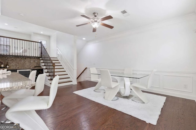 dining area with visible vents, ceiling fan, wainscoting, a decorative wall, and dark wood-style flooring