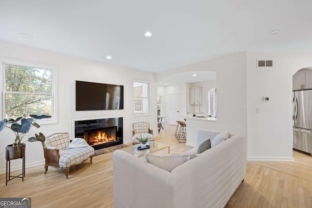 living room featuring visible vents, a glass covered fireplace, arched walkways, light wood-style floors, and baseboards