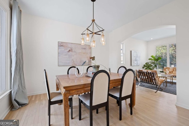 dining area featuring light wood-type flooring, arched walkways, baseboards, and a chandelier