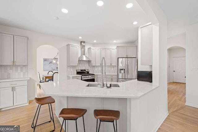 kitchen featuring a breakfast bar, a peninsula, arched walkways, appliances with stainless steel finishes, and wall chimney range hood