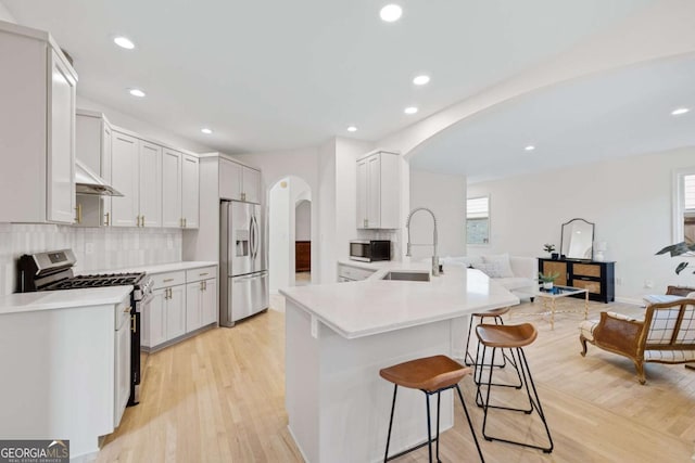 kitchen featuring a sink, open floor plan, stainless steel appliances, arched walkways, and a breakfast bar area