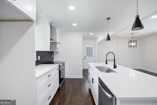 kitchen with dark wood finished floors, a kitchen island with sink, a sink, decorative backsplash, and appliances with stainless steel finishes